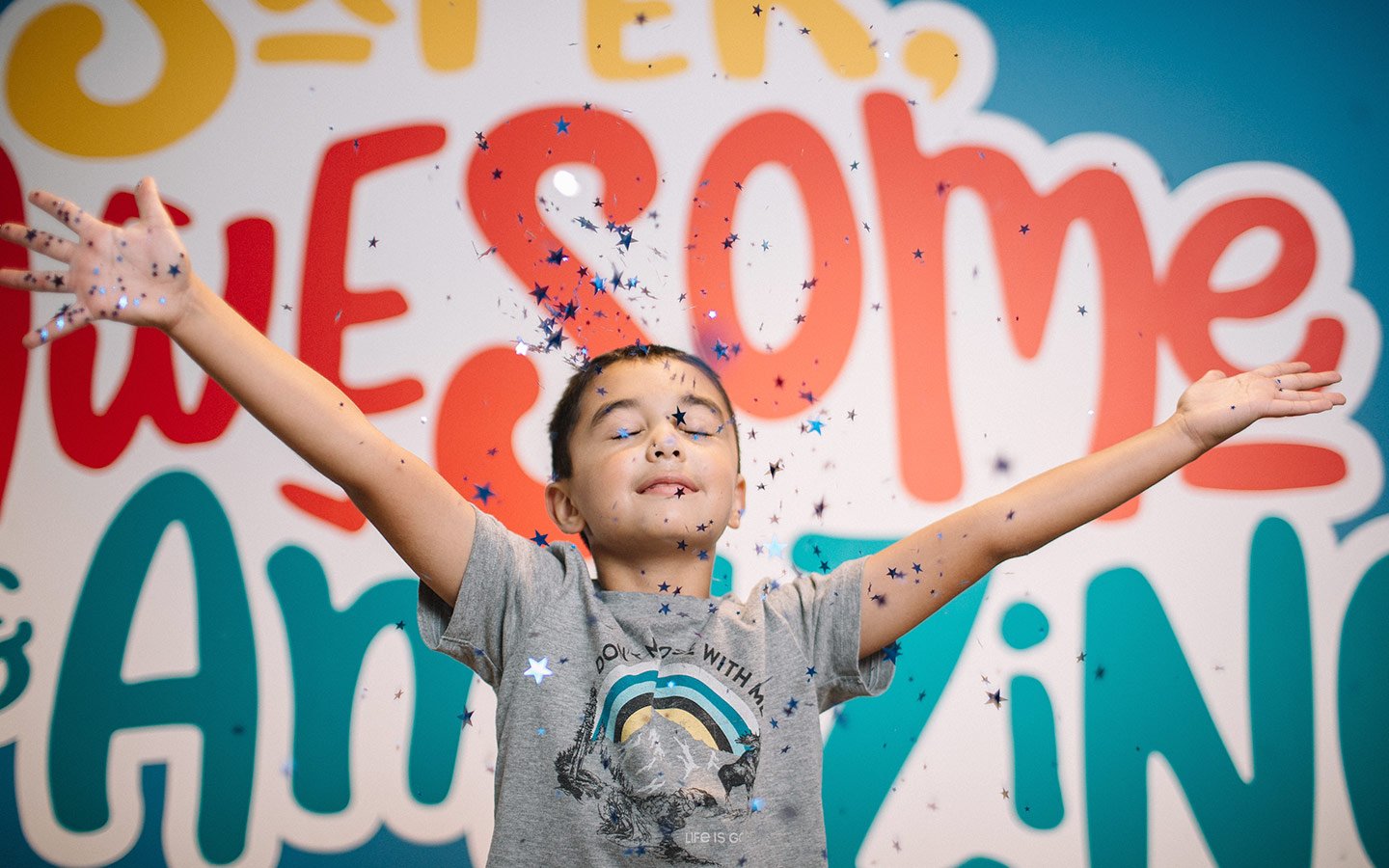 Boy with arms outstretched smiling as confetti falls.
