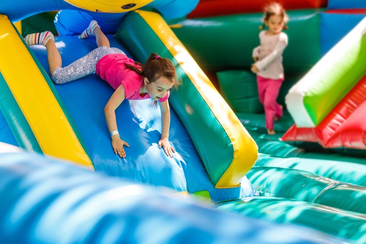 Young girl sliding down bouncy house slide in brightly lit room